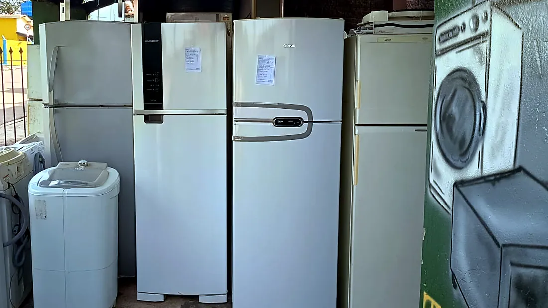 Geladeiras enfileiradas, cada uma com uma ficha de papel na porta, ao lado de um grafite de máquina de lavar
