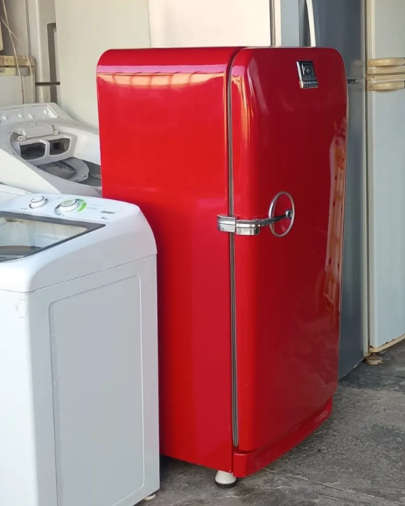 Geladeira antiga vermelha ao lado de uma máquina de lavar, na loja